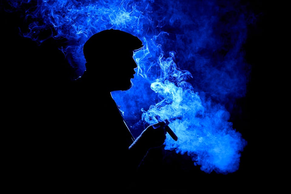 When you learn photography, you can take beautiful pictures like this, using a flash and colored lights. This example photo shows the backlit silhouette of a man smoking a cigar.