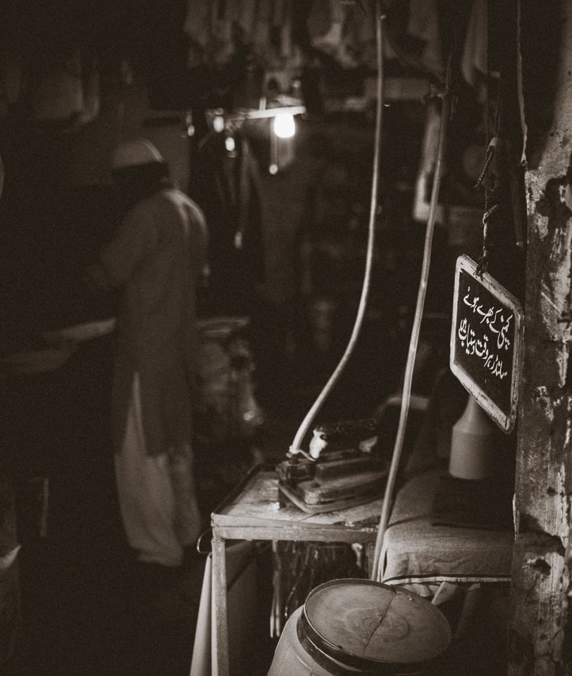 Tailor busy at work. According to the sign at the entrance, the shop also sells gas cylinders (to supplement the village's intermittent supply).