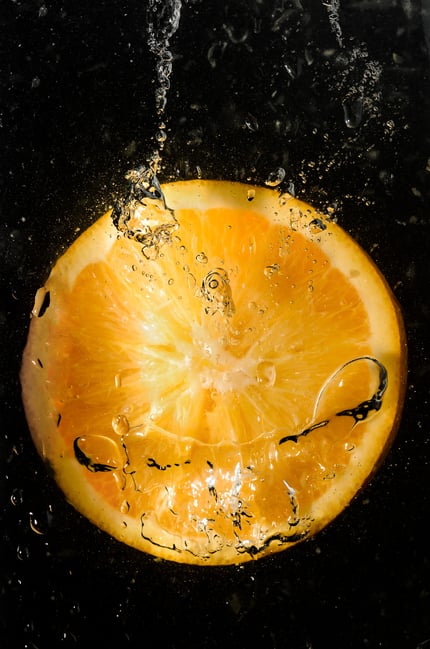 Orange slice falling into water with bubbles