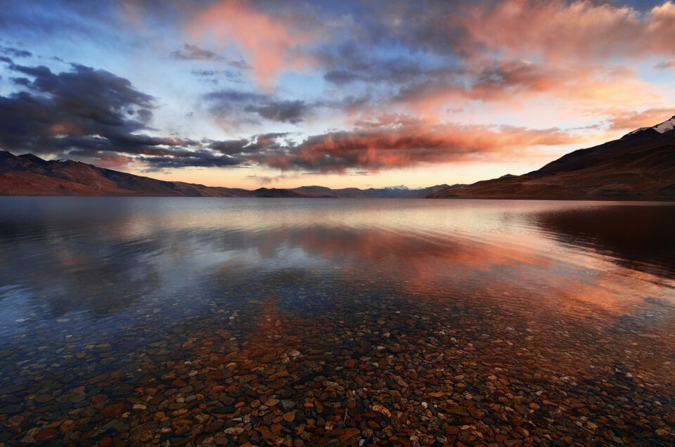 Sebuah pantulan sebuah danau saat matahari terbenam dengan awan berwarna-warni - cara menangkap foto-foto refleksi
