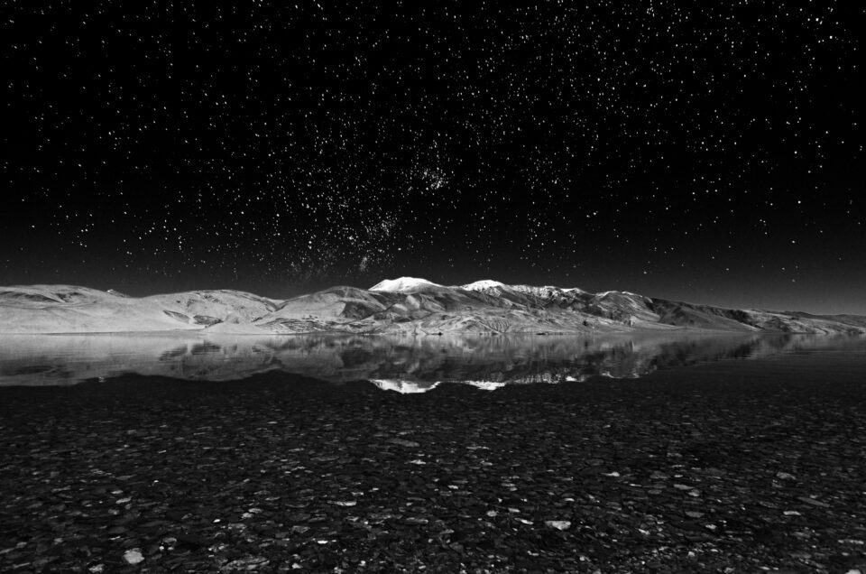 A black and white image of a lake at night with stars