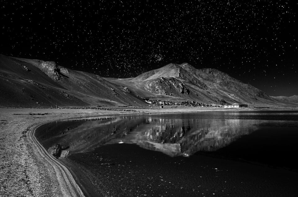 A lake reflection at night with mountains and stars